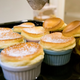 Eight miniature homemade souffles being dusted with powdered sugar on countertop